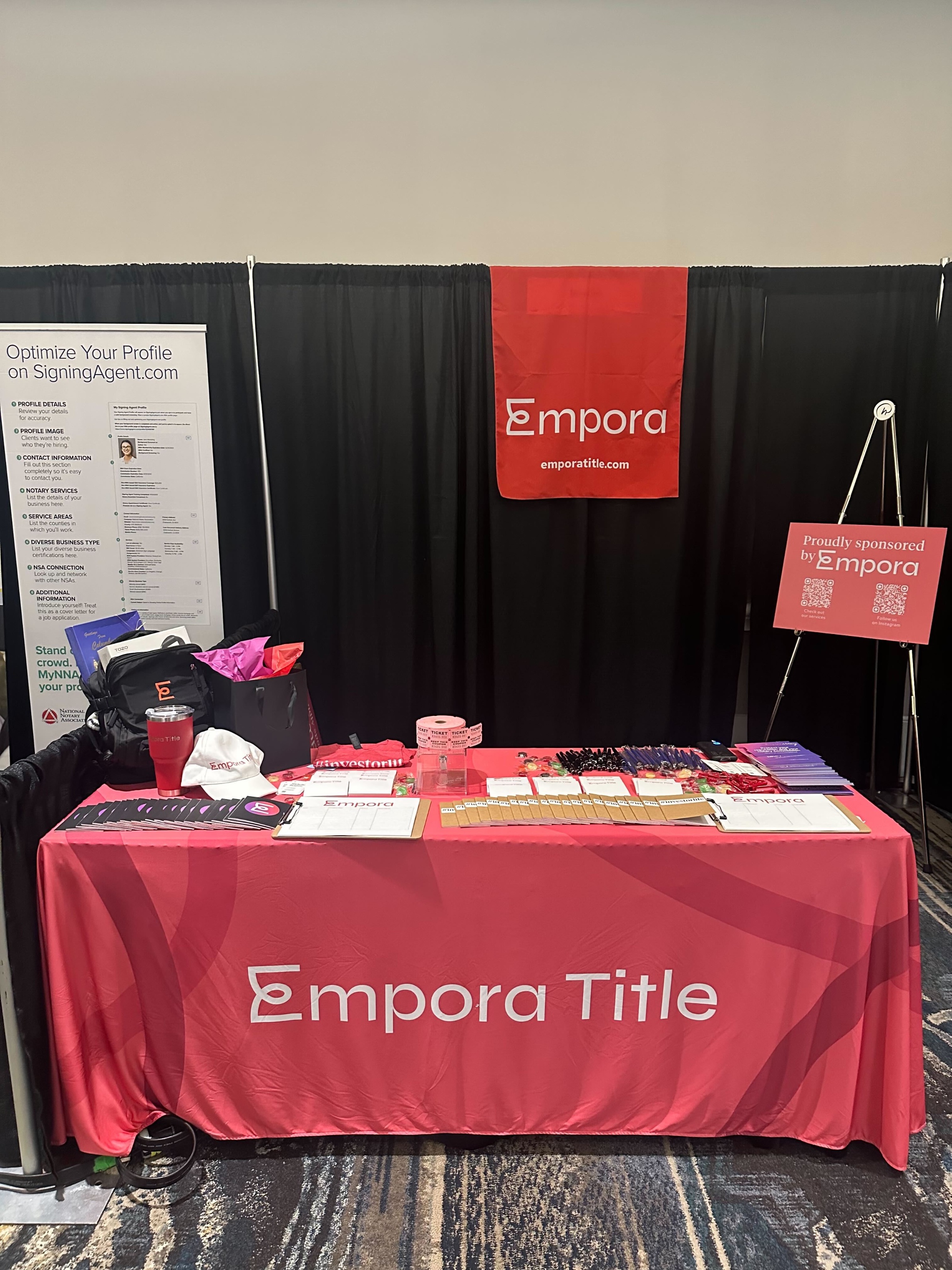 The Empora booth at NNA: a Garnet-red tablecloth with the Empora wordmark, a hanging banner, and a 'Proudly sponsored by Empora' sign at the corner.